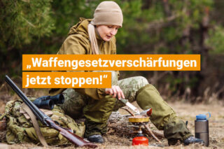 Frau im Wald schiebt Ihr Fleisch mit einem Messer auf einem Gaskocher herum. Neben Ihr lehnt ein Gewehr